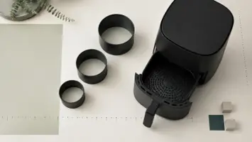 Åpen, umerket airfryer med perforert kurv og kapasitetssirkler på et lyst måleark
